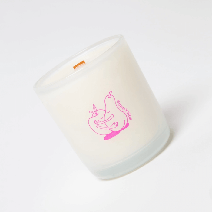 Close-up angled view of Milkjar Sunnyside candle in frosted glass with wooden wick and pink pear and nectarine icon.