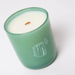 Milkjar Woodland essential oil candle in green glass photographed at an angle on a white background with wooden wick.