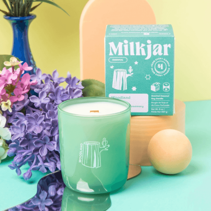 Milkjar Woodland green glass candle and box styled with flowers and pastel props for a fresh spa-inspired look.