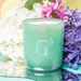 Milkjar Woodland essential oil candle in green glass with wooden wick, styled with lilac and white flowers.