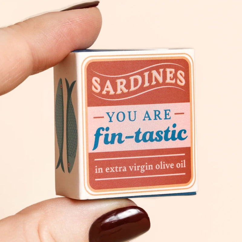 Hand holding sardines themed matchbox that reads You are fin-tastic, with fish illustration on side