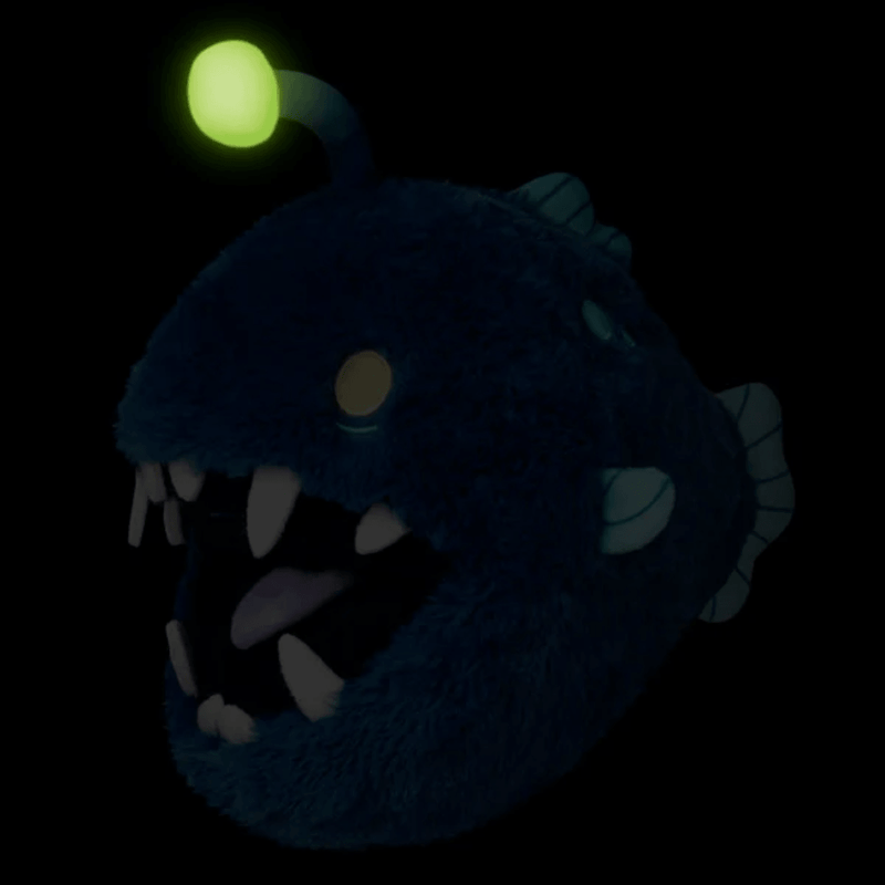 Mini Squishable Anglerfish plush in darkness with its glowing yellow lure illuminated