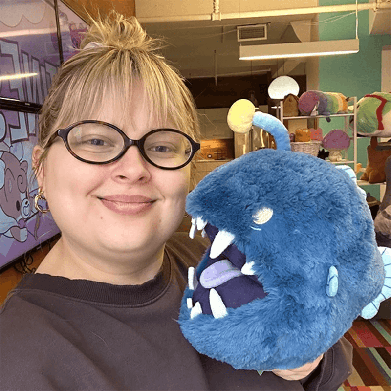 Person holding Mini Squishable Anglerfish plush showing its fluffy blue body and oversized toothy mouth