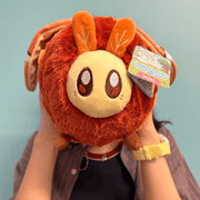 Mini Squishable Atlas Moth plush being held with its cream face and orange body visible
