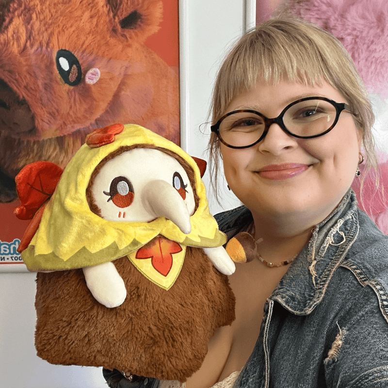 Person holding Mini Squishable Autumn Fairy Plague Nurse plush showing its fluffy brown body and autumn outfit
