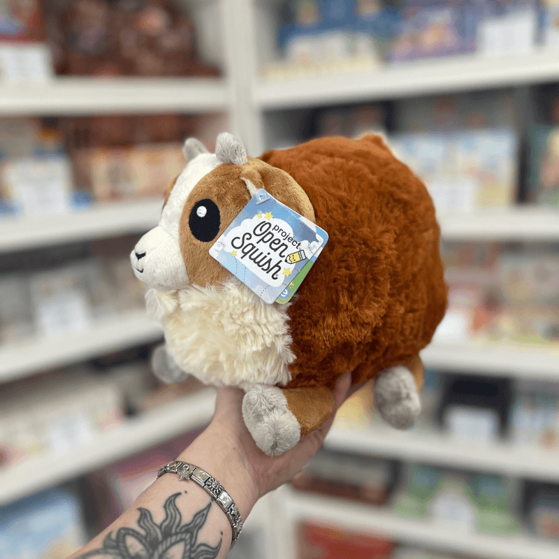 Mini Squishable Baby Goat plush toy held in hand, angled view showing the rounded body, soft brown plush fur, cream face and fluffy chest detail