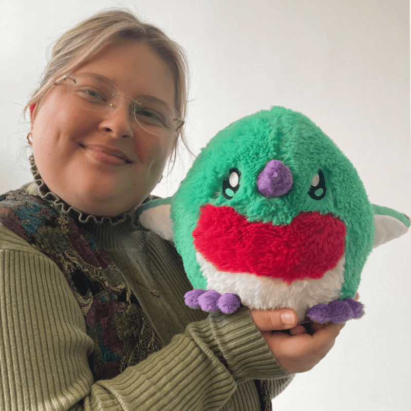 Person holding Mini Squishable Baby Hummingbird plush toy in green, red and purple.