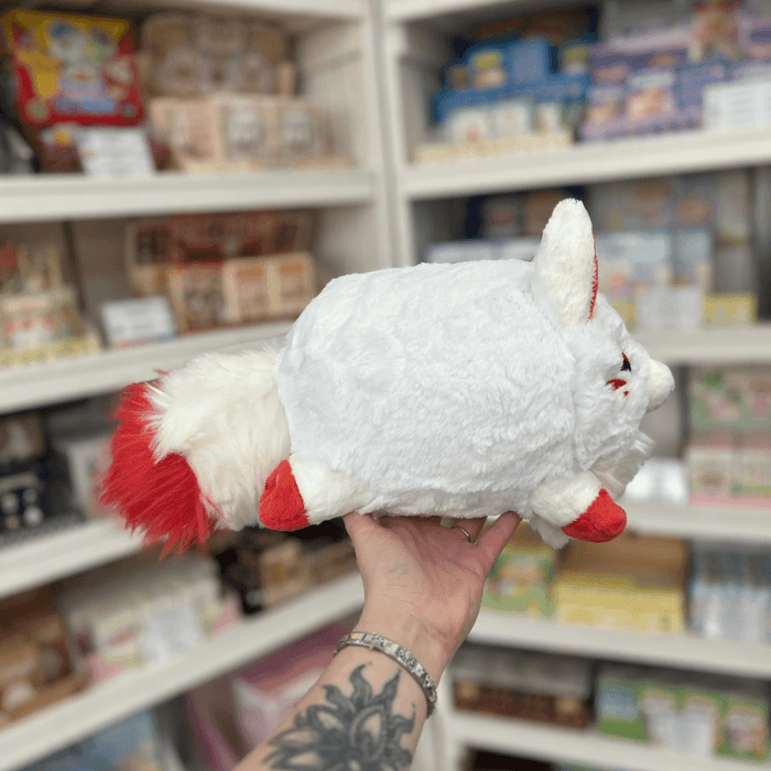 Side view of Mini Squishable Baby Kitsune plushie showing its white fluffy body, red ears, red feet and fox face