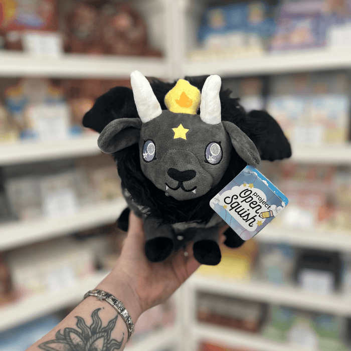 Mini Squishable Baphomet plush toy held in hand, front view showing the dark grey face, white horns, yellow crown, silver eyes and black wings