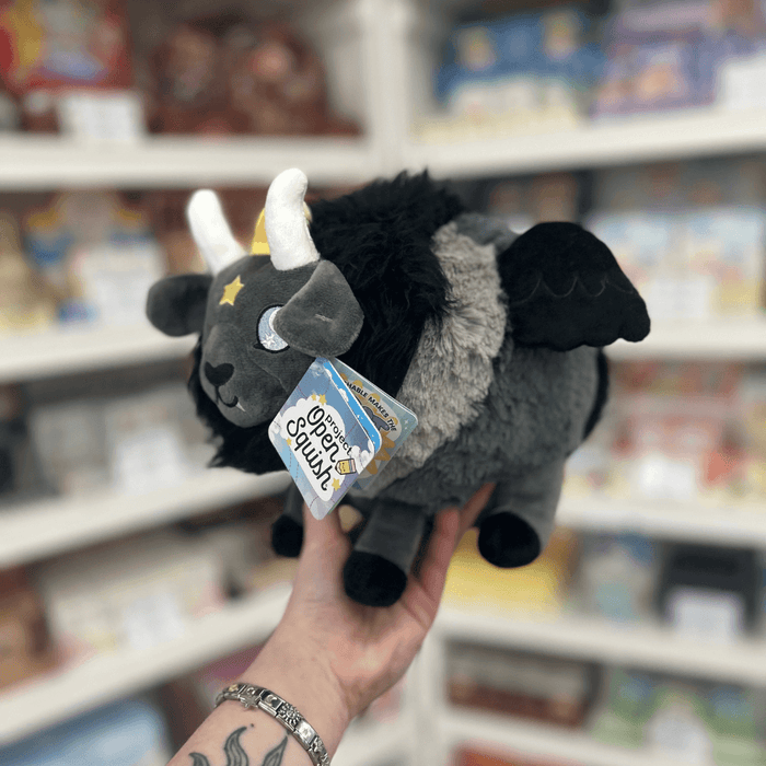 Mini Squishable Baphomet plush toy held in hand, angled side view showing the black mane, grey body, black wings, white horns and soft plush details