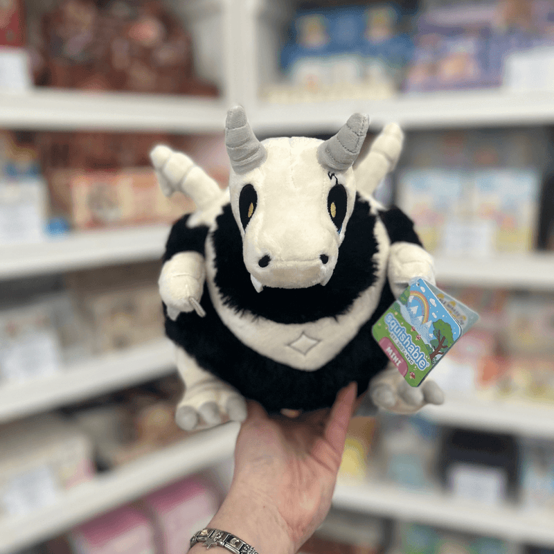 Mini Squishable Bone Dragon plush toy held in hand, front view showing the white dragon skull face, grey horns, little fangs and black fluffy body