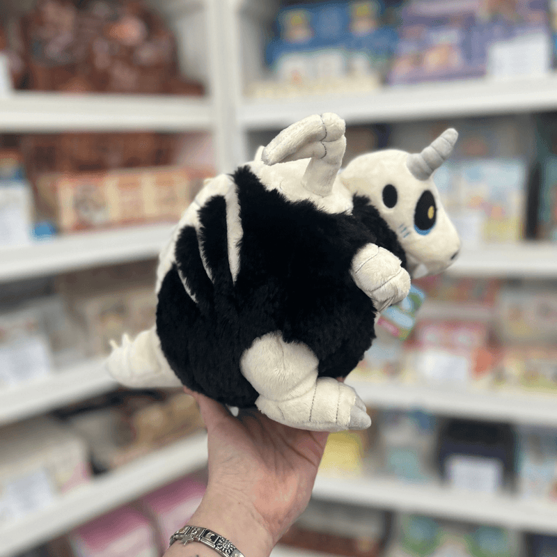 Mini Squishable Bone Dragon plush toy held in hand, rear side view showing the fluffy black body, pale wings, striped spine detail and curled tail