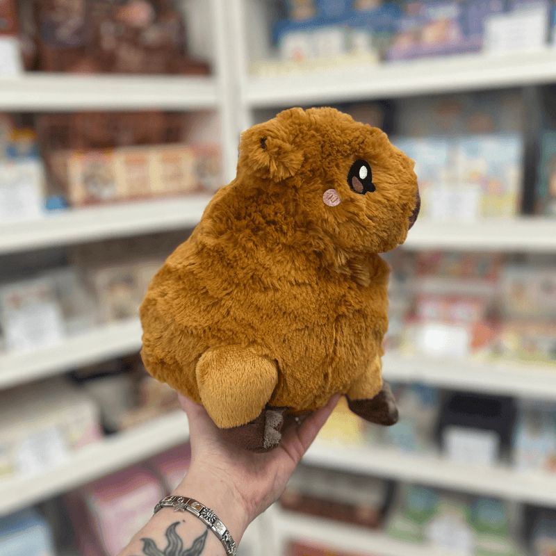 Mini Squishable Capybara plush toy held in hand, side view showing the soft brown plush body, embroidered eye, rounded snout and little feet