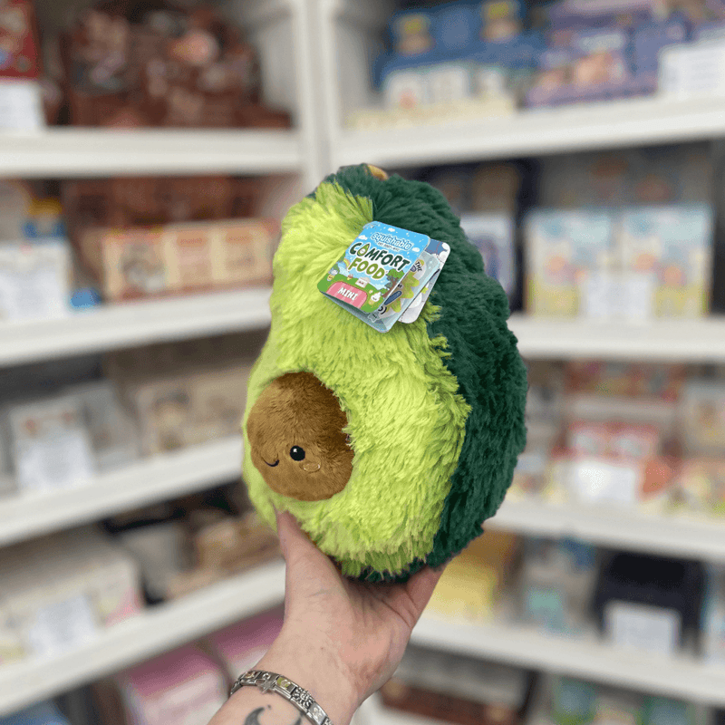 Mini Squishable Comfort Food Avocado plush toy held in hand, angled view with tag visible