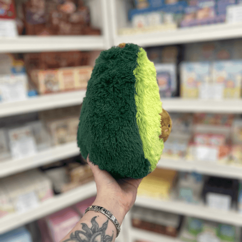 Mini Squishable Comfort Food Avocado plush toy held in hand, side view showing dark green back and soft plush texture