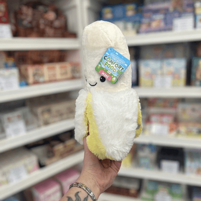 Mini Squishable Comfort Food Banana plush toy held in hand, angled view showing the soft white banana top and fluffy yellow peel