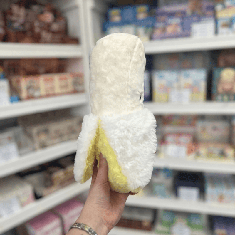 Mini Squishable Comfort Food Banana plush toy held in hand, side view showing the peeled banana shape and plush yellow peel detail