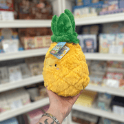Mini Squishable Comfort Food Pineapple plush toy held in hand, angled view showing the cheerful face, textured yellow plush body and leafy green top