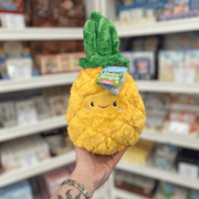 Mini Squishable Comfort Food Pineapple plush toy held in hand, front view showing the smiling pineapple face and soft green leaves