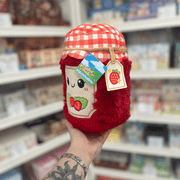 Mini Squishable Comfort Food Strawberry Jam plush toy held in hand, angled view showing the soft red jam jar, gingham lid and strawberry gift tag