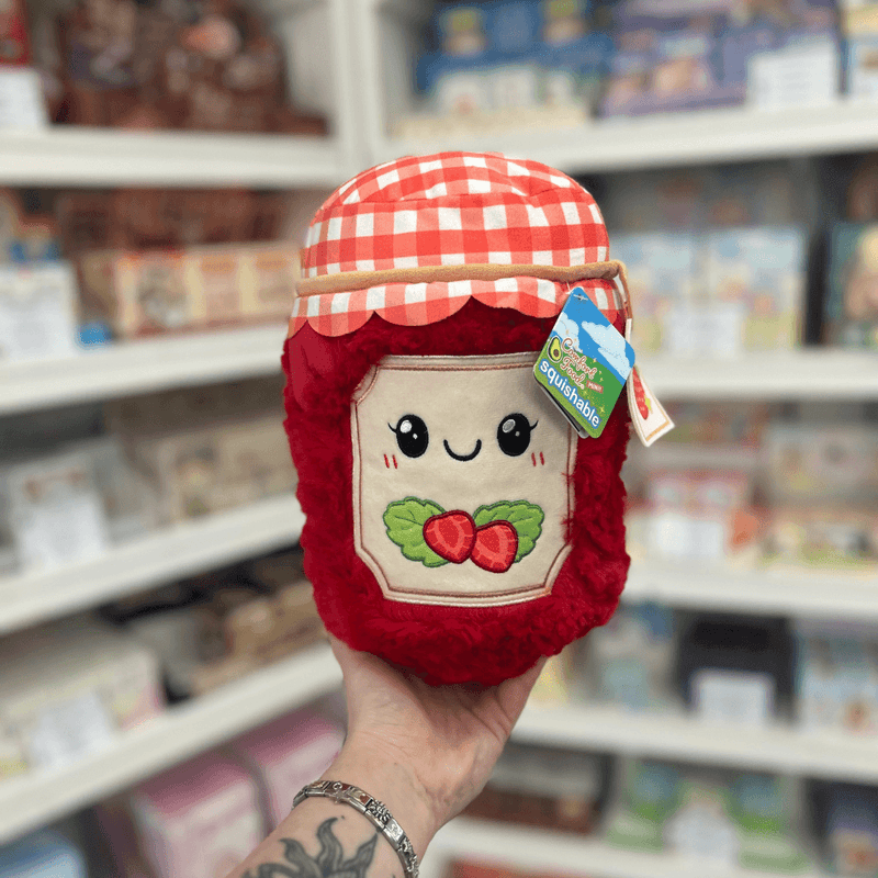 Mini Squishable Comfort Food Strawberry Jam plush toy held in hand, front view showing the smiling jam jar design with gingham lid