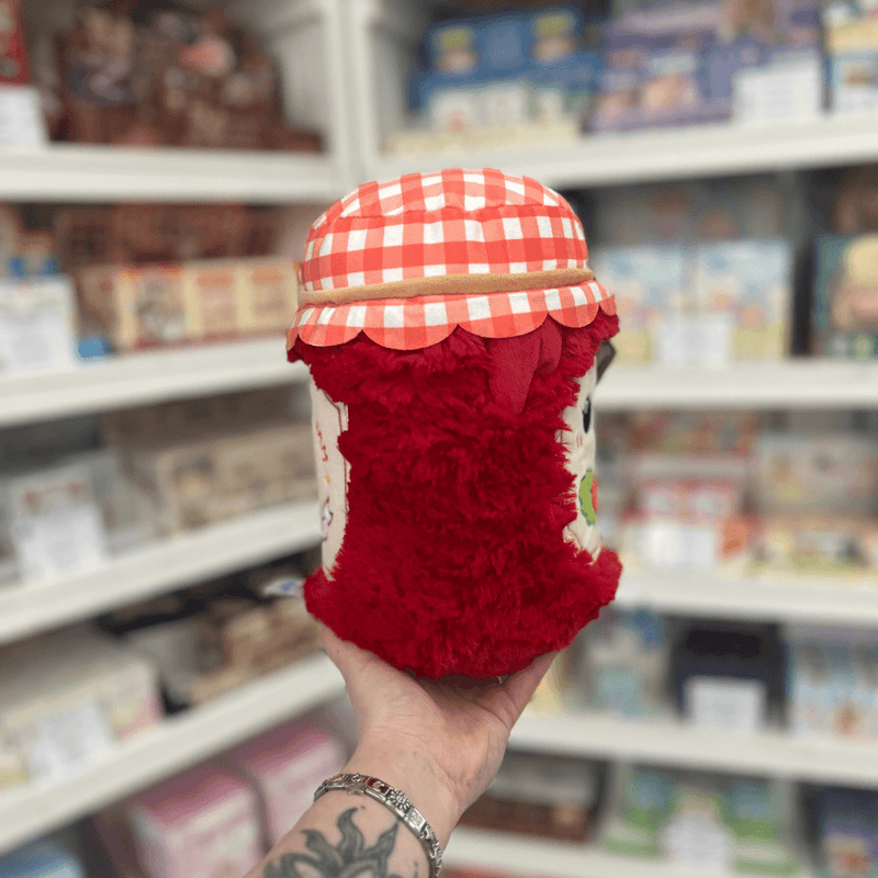 Mini Squishable Comfort Food Strawberry Jam plush toy held in hand, side view showing the fluffy red jar shape and gingham lid detail