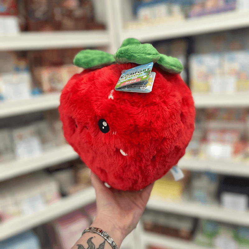 Mini Squishable Comfort Food Strawberry plush toy held in hand, angled view showing the cheerful face, plush strawberry shape and soft green leaf detail