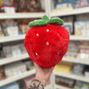 Mini Squishable Comfort Food Strawberry plush toy held in hand, back view showing the rounded red plush strawberry shape, embroidered seed details and green leafy top