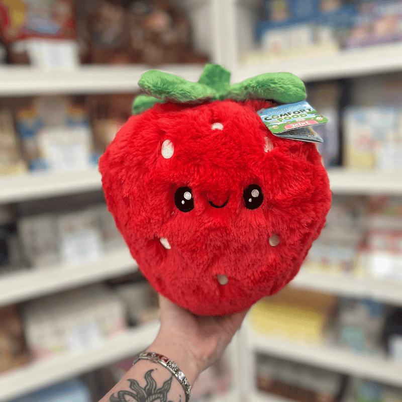 Mini Squishable Comfort Food Strawberry plush toy held in hand, front view showing the smiling strawberry face, soft red plush fabric and green leafy top