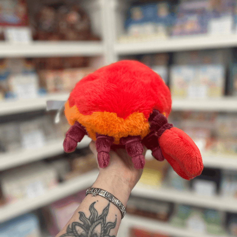 Mini Squishable Crab plush toy held in hand, rear view showing the fluffy red shell, orange lower edge, soft legs and one raised claw