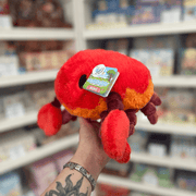 Mini Squishable Crab plush toy held in hand, angled side view showing the rounded red shell, stitched smile, chunky claw and soft segmented legs