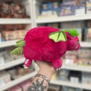 Mini Squishable Dragon Fruit plush toy held in hand, side and rear view showing the bright pink plush body, green wings, tail and soft dragon fruit-inspired design