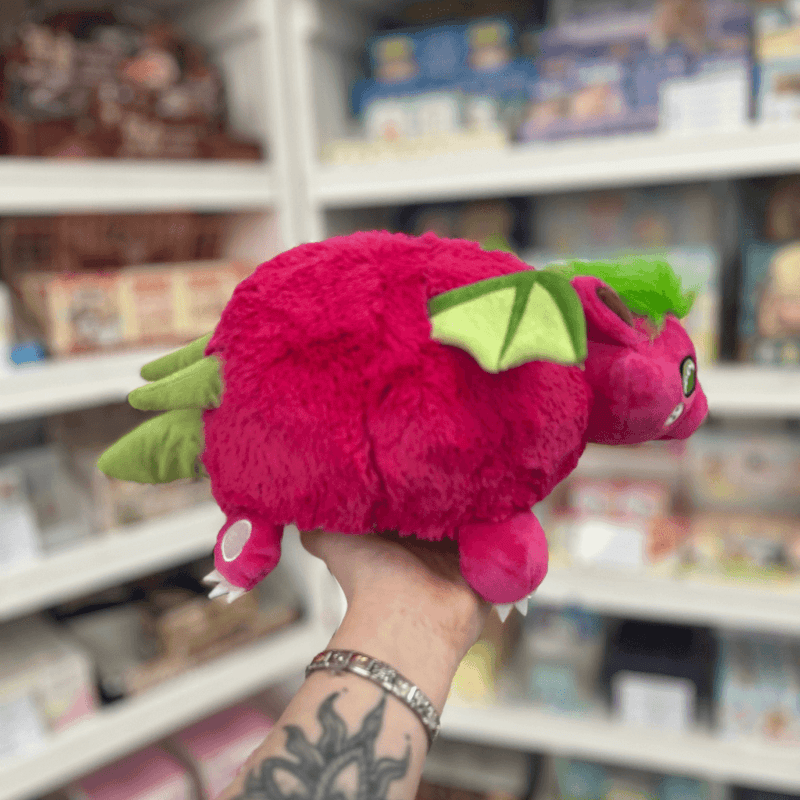 Mini Squishable Dragon Fruit plush toy held in hand, side and rear view showing the bright pink plush body, green wings, tail and soft dragon fruit-inspired design
