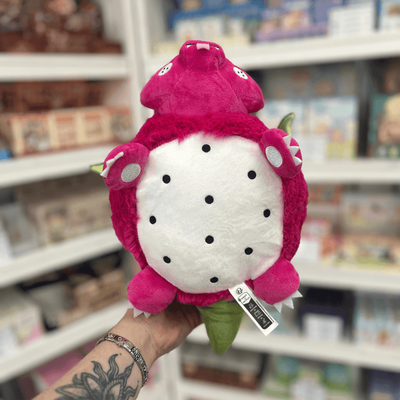 Mini Squishable Dragon Fruit plush toy held upside down in hand, showing the white dragon fruit-style belly with black seed details, pink paws and green tail
