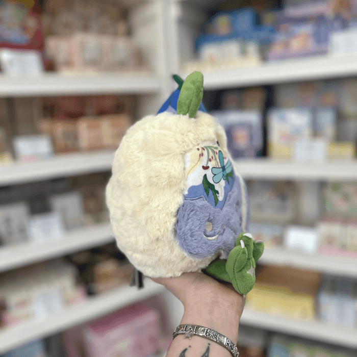 Side view of Mini Squishable Fairy Baby Mothman plushie with fluffy cream fur, floral wing detail and green feet