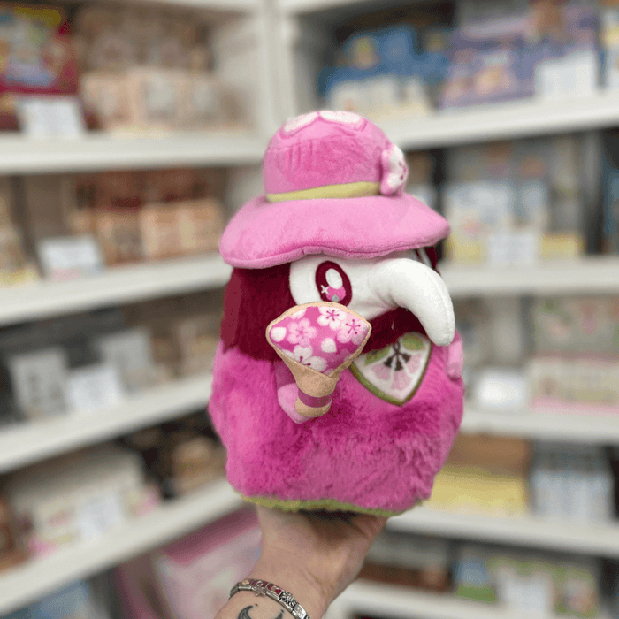 Mini Squishable Sakura Plague Doctor plush toy held in store, showing its pink plush body, beak mask and cherry blossom accessory