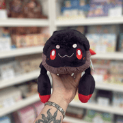 Mini Squishable Scorpion plush toy held in hand, front view showing the black body, red eyes, soft smile and red-tipped claws