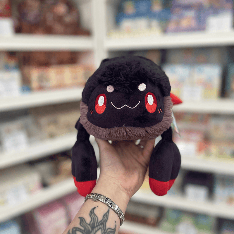 Mini Squishable Scorpion plush toy held in hand, front view showing the black body, red eyes, soft smile and red-tipped claws