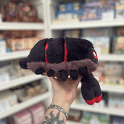 Mini Squishable Scorpion plush toy held in hand, side profile showing the black segmented body, small legs, red band detailing and oversized red-tipped claw