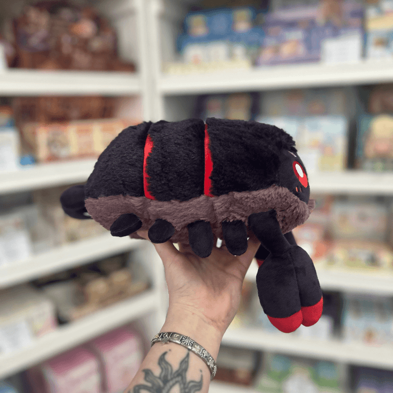 Mini Squishable Scorpion plush toy held in hand, side profile showing the black segmented body, small legs, red band detailing and oversized red-tipped claw