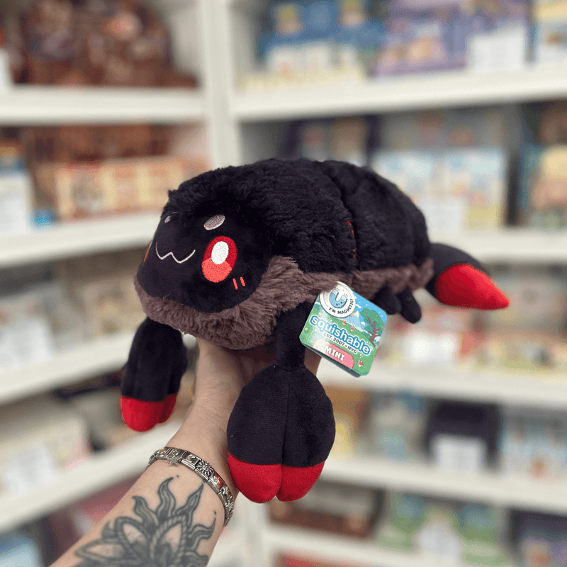Mini Squishable Scorpion plush toy held in hand, angled side view showing the segmented black body, fluffy grey trim, red-tipped claws and curved tail