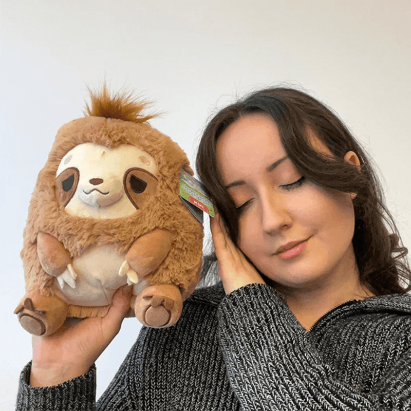 Person holding Mini Squishable Sleepy Sloth plush toy next to their face.