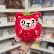 Mini Squishable Strawbeary plush toy held in hand, front view showing the bright red berry-inspired fur, pink face, embroidered features and leafy top