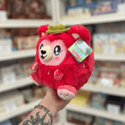 Mini Squishable Strawbeary plush toy held in hand, angled side view showing the soft red plush body, pink paws, embroidered face and green leaf detail on top