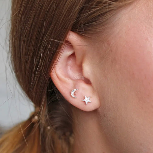 Close-up of silver moon and star crystal stud earrings worn on ear