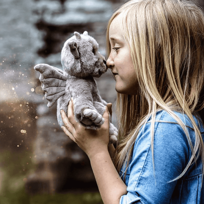 Child cuddling Moat grey dragon plush from Bearhouse by Charlie Bears, showing soft wings, horns and plush face
