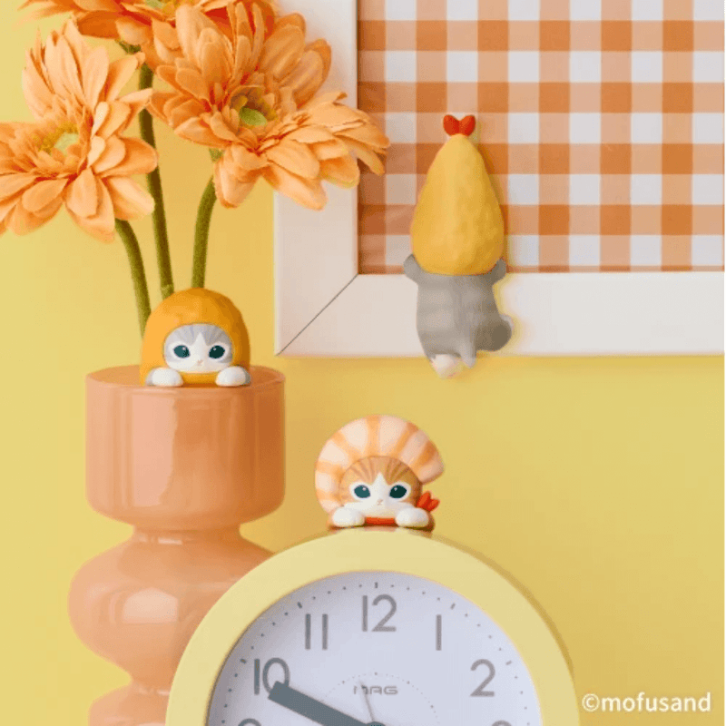 Mofusand shrimp cat figures peeking over a desk clock