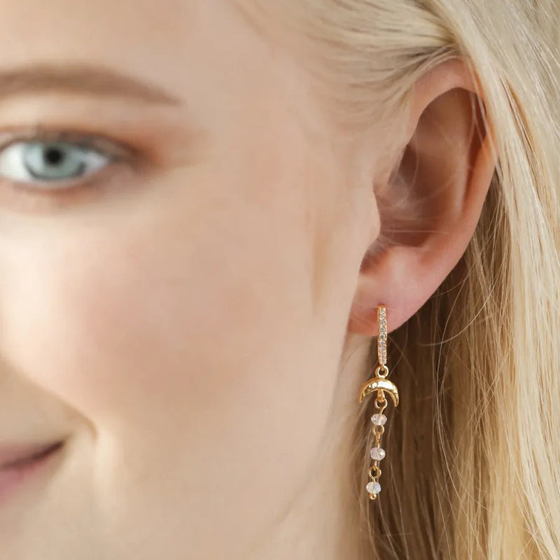 Gold crescent moon and crystal drop huggie earring worn in the lobe for a sparkly celestial look.