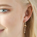Gold crescent moon and crystal drop huggie earring worn in the lobe for a sparkly celestial look.