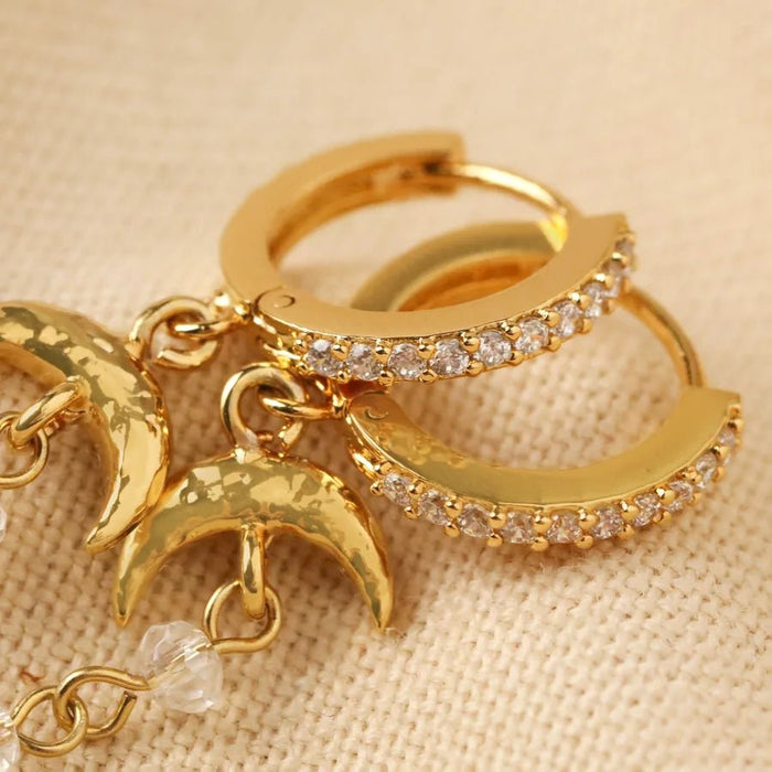 Close-up of gold pavé huggie hoops showing click hinge and textured crescent moon charms with crystal beads.